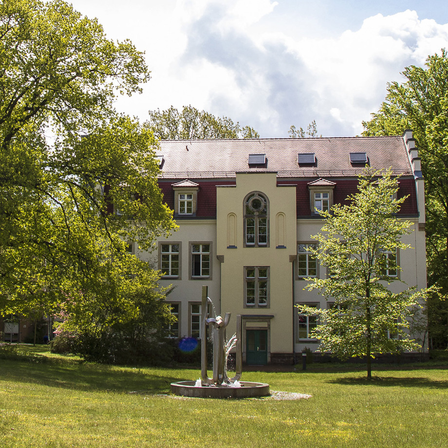 Ein dreistöckiges Gebäude mit einem grünen Rasen und Bäumen im Vordergrund.