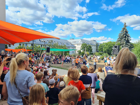 Große Menschenmenge bei einem Freiluft-Event, mit Kindern im Vordergrund.